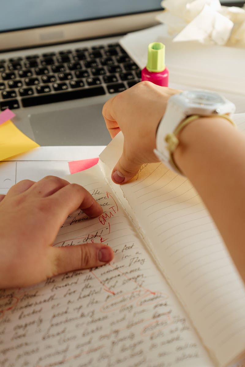 Hands tearing a page from a notebook with a laptop in the background on a workplace desk.